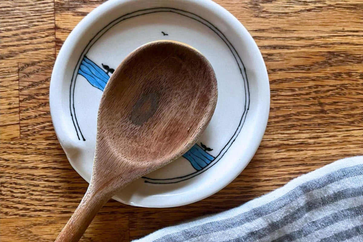 Wooden spoon on a white spoon rest with hand-drawn blue waves and whales diving underneath