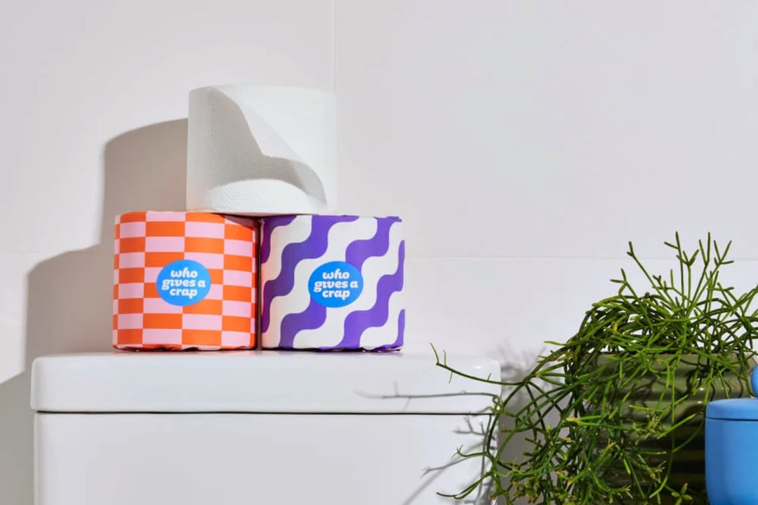 100% Post-Consumer Recycled Toilet Paper sitting on toilet tank in white bathroom